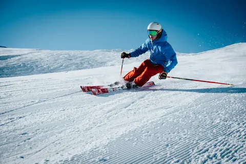 Skier carving a turn on a groomed slope in bright sun